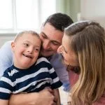 Family photo of mother and father embracing their disabled son in relation to in-home support